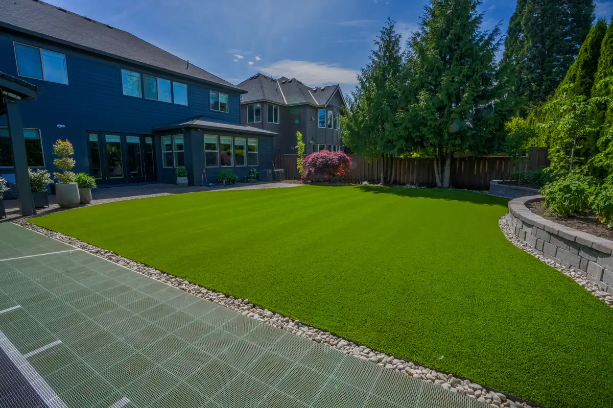 Large backyard with artificial turf paver patio and retaining wall by CreekView Landscape